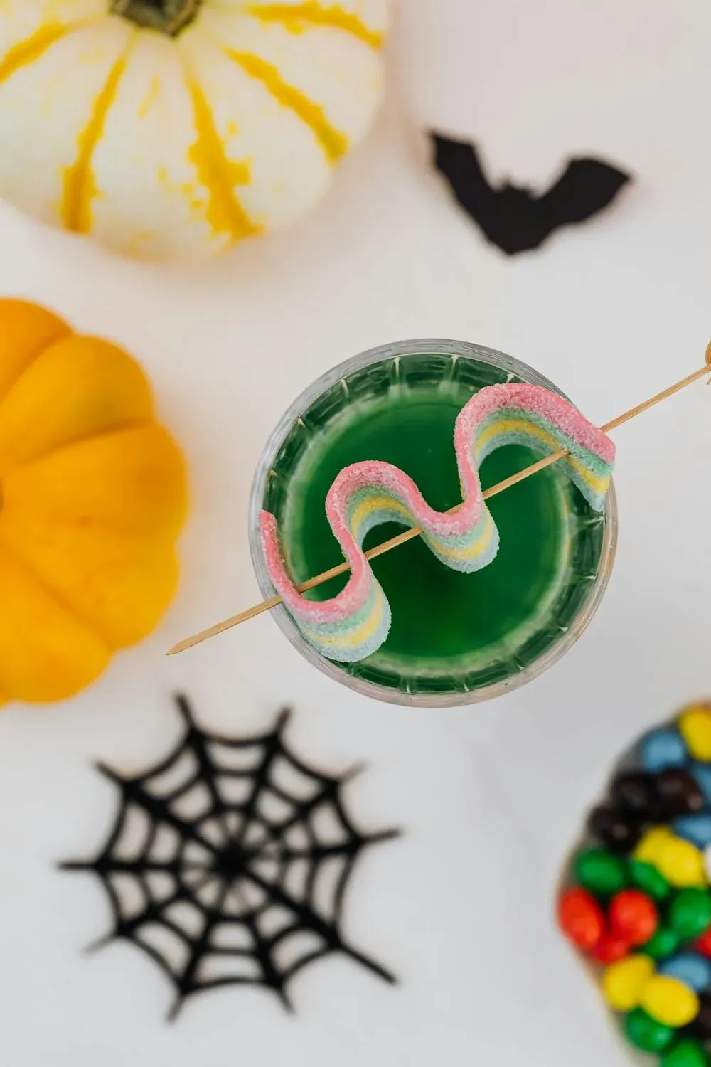 A sugar coated candy on stick laying over an halloween drink.