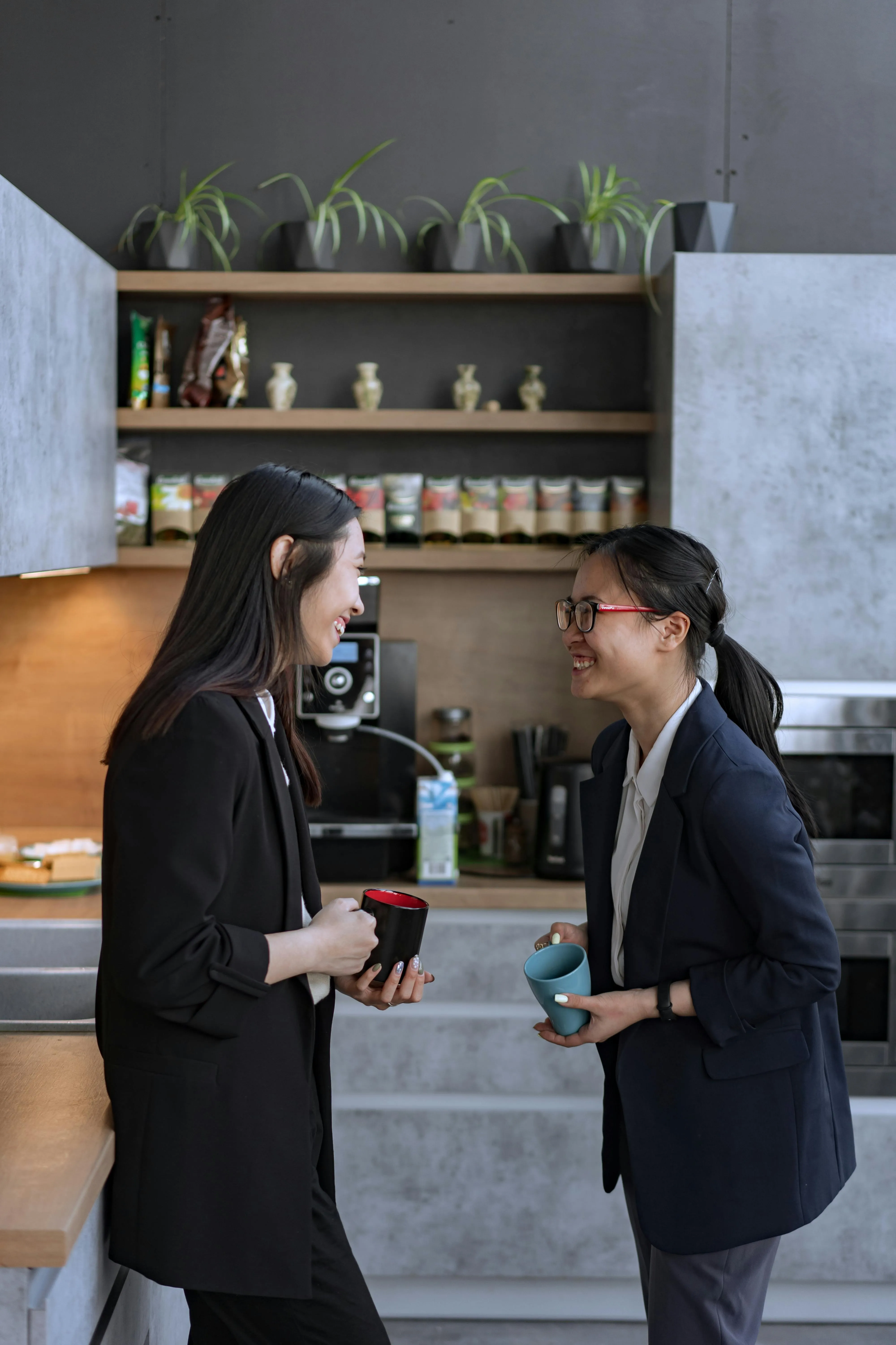 Zwei Männer stehen mit ihren Lattes vor der Kaffeemaschine im Büro. Ihr glückliches Aussehen vermittelt ein Bild von Freude und Zufriedenheit. Dies zeigt, wie Freundschaften unter Kollegen einen positiven Einfluss auf das Arbeitsklima haben können.